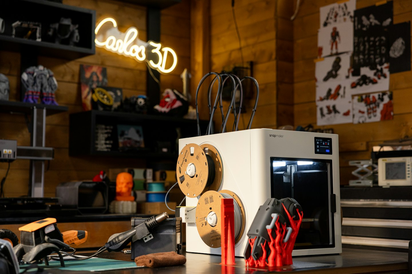 Šiuolaikinis 3D spausdintuvas, gaminantis raudoną objektą ant darbastalio.